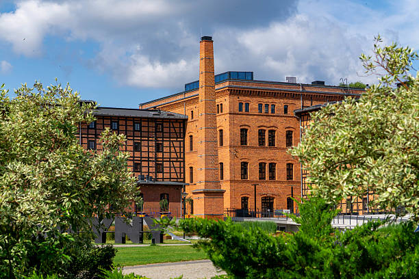 Revitalized Rother's Mills building in Bydgoszcz, surrounded by greenery under a blue sky.