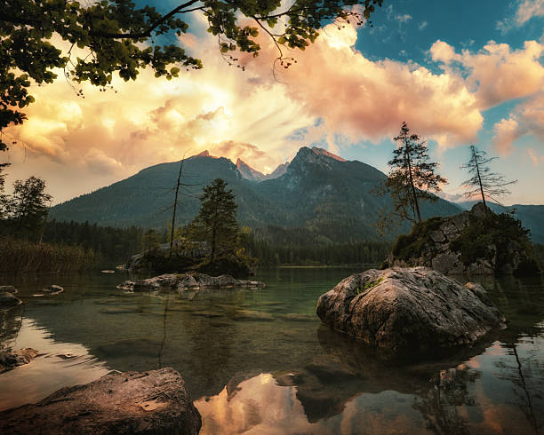 Golden clouds at sunset over the Watzmann mountains and Hintersee lake in the German Alps. Lakeshore landscape with dramatic sky.
