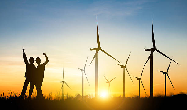 istock Silhouette two female engineers working outdoors wind turbine power station raising their fists to the sky in joy at the start of work in the morning at sunrise amidst a beautiful windmill field. 2228454986