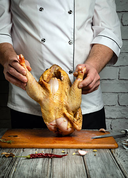istock A chef holds a whole chicken upside down, ready for preparation, while surrounded by fresh herbs and spices on a wooden cutting board in a traditional kitchen setting 2228456081