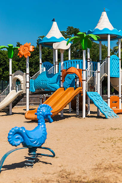istock A lively playground features orange and blue slides, climbing structures, and playful decorations, surrounded by greenery under a clear blue sky during the day 2228456328