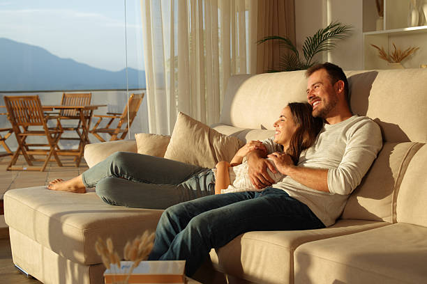 Happy couple at sunset at home looking through a window stock photo