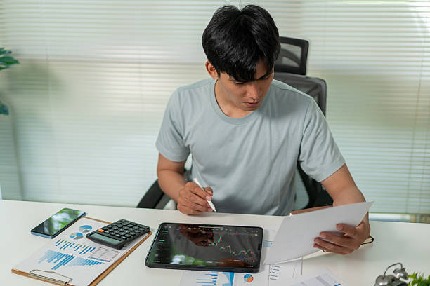 istock Asian man holding smartphone, analyzing investment trading data on crypto chart with smartphone and laptop while working at home. Cryptocurrency, Bitcoin, Digital ledger. 2228459764