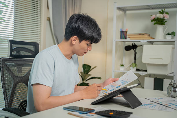 istock Asian man holding smartphone, analyzing investment trading data on crypto chart with smartphone and laptop while working at home. Cryptocurrency, Bitcoin, Digital ledger. 2228460327