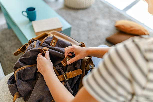 istock Young woman organizes her backpack in a cozy indoor setting while seated on a sofa 2228468329