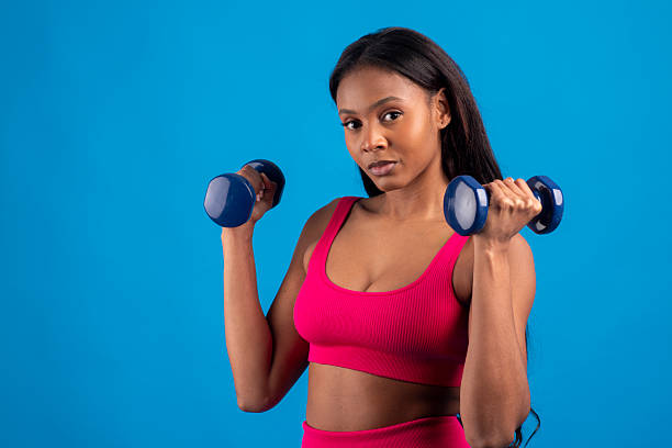 istock Young black woman lifting weights on blue background 2228468710
