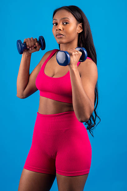 istock Young black woman lifting weights on blue background 2228468884