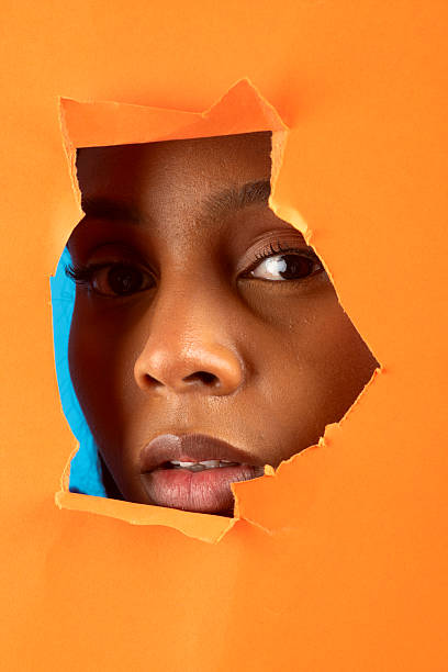 istock Curious young woman peeking through torn orange paper 2228469995