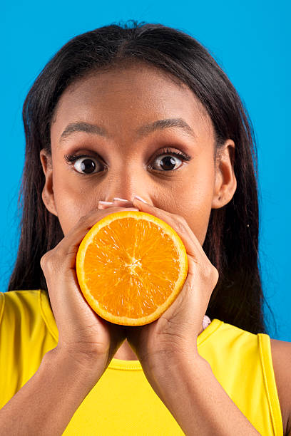 Young woman holding an orange slice in front of her face with a surprised expression