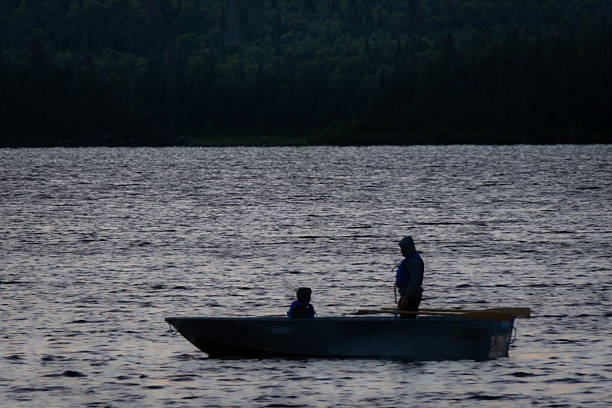 A man and his young son sit peacefully on a small boat, surrounded by the tranquil waters of the lake.