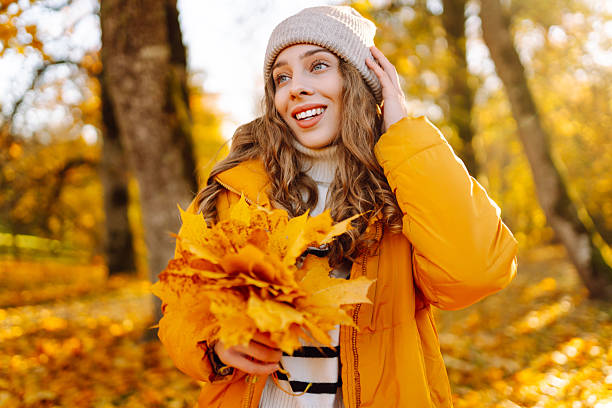 istock A cheerful woman in a bright jacket collects and throws bright foliage in a sunny park. 2228472425