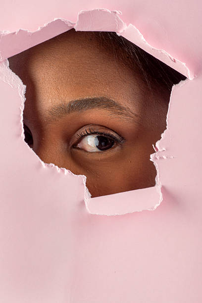 istock Curious young woman peeking through torn pink paper hole 2228476092