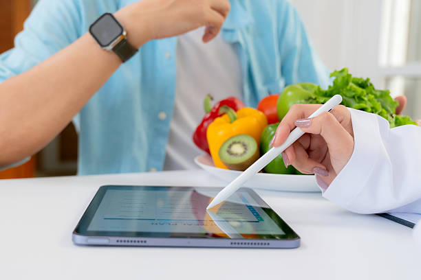 istock Asian nutritionist using tablet to explaining personalized meal plan with AI to patient during healthcare consultation, healthy lifestyle, woman dietitian showing nutrition plan with AI on tablet. 2228476679