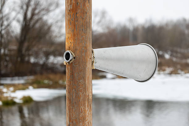 Metal gaming hearing trumpet on a wooden pole outdoors. The hearing horn is designed for use in children's science parks to listen to the sounds of wild nature.