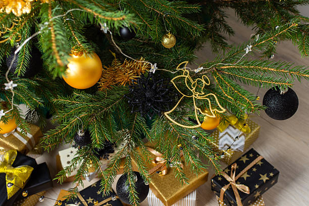 Luxurious gold and black gift boxes arranged beneath a Christmas tree, illuminated by glowing candles and adorned with elegant decorations, creating a chic holiday ambiance