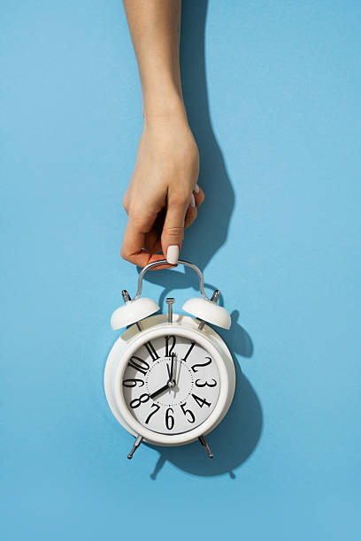 istock Woman hand holding white clock on blue background 2228481089