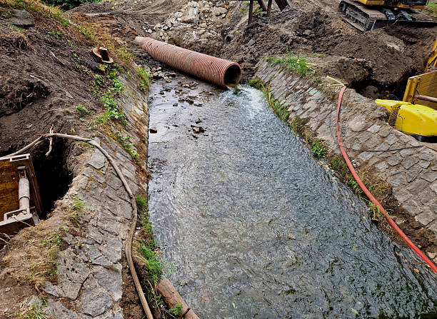 istock construction of flood control measures where half of the stream is diverted into a pipe. temporary embankment made of loose earth. stone blocks are set into concrete and create a weir, aerial view 2228482247