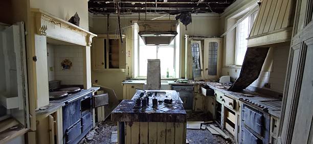 istock Old-fashioned kitchen burned. Natural sunlight through window, fire damaged central island counter and open burned drawers. Aga oven cooker with charred surfaces from arson or accident 2228482417