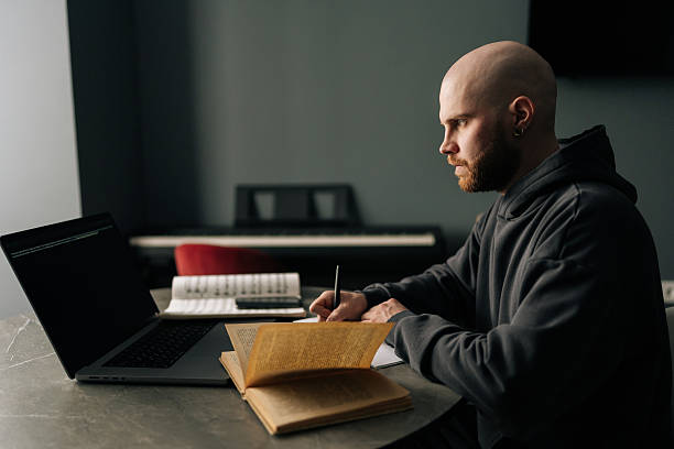 istock Focused talented composer writing music notes on paper sitting at table with laptop, books, sheet music in home office, immersing in creativity and inspiration. 2228484794