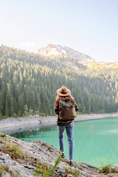 istock A back view of a female hiker in a hat and with a backpack sitting on a rock overlooking a high mountain lake. 2228486883