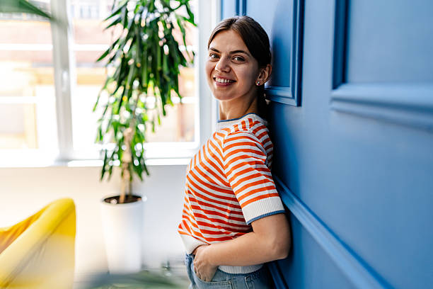 istock Young woman smiling while leaning against a vibrant blue wall in a bright, modern indoor space during the day 2228491442