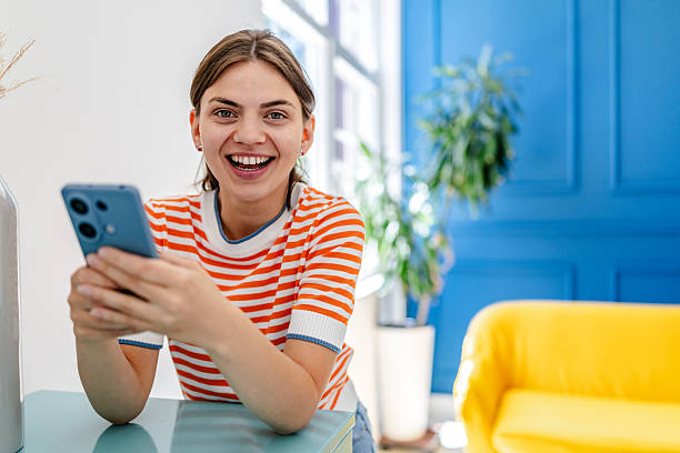istock Young woman smiling while using her smartphone in a bright indoor setting with blue and yellow accents 2228491609