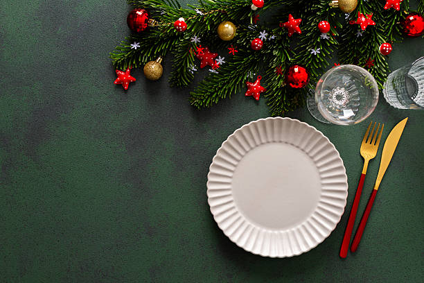 istock Elegant Christmas table setting with an empty plate and cutlery on a deep green surface. Red Christmas decorations and spruse branches add a warm, holiday touch 2228492416