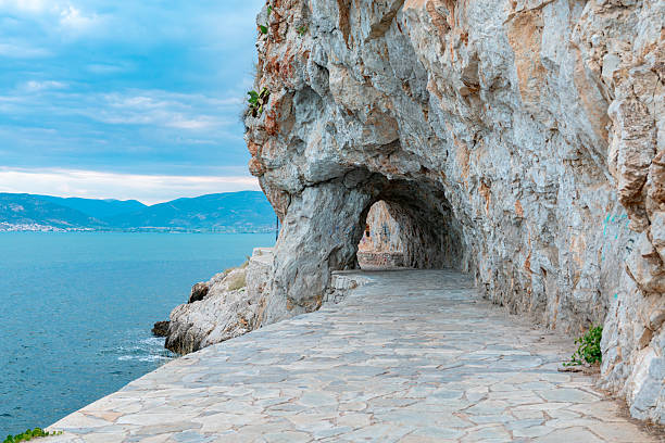 Scenic cobblestone path near Nafplio, Greece, winding between rocky cliffs and the Acronafplia fortress. A picturesque blend of natural beauty and ancient architecture in the Peloponnese.