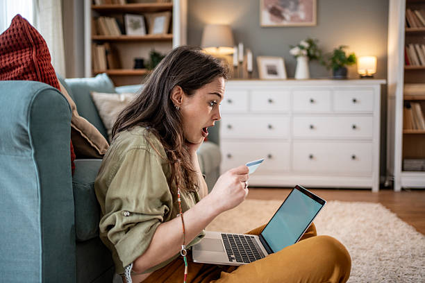 istock Shocked young woman looking at credit card while using laptop at home 2228493540