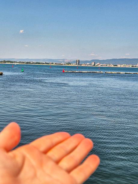 istock a person's hand reaching towards  the sea on a sunny day. 2228501921