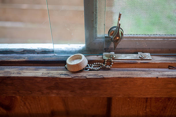 A close view of a window in an old house shows peeling paint on the sill and a small potted plant. Sunlight streams in, illuminating the wear and tear of the environment.