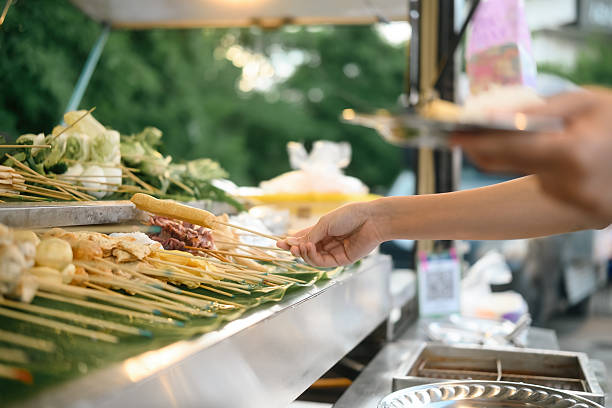Close-up of a hand selecting skewered ingredients at a street food stall, featuring fresh vegetables and meats ready for grilling at a MALA Chinese BBQ food truck