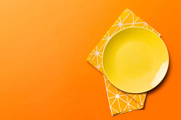 Top view on colored background empty round yellow plate on tablecloth for food. Empty dish on napkin with space for your design.