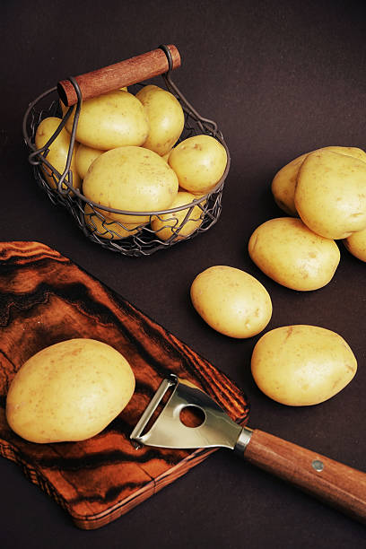 istock Potatoes on board near vegetable peeler on dark background 2228516998