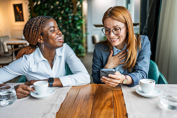 istock Businesswomen laughing while looking at smartphone in cafe 2228517625