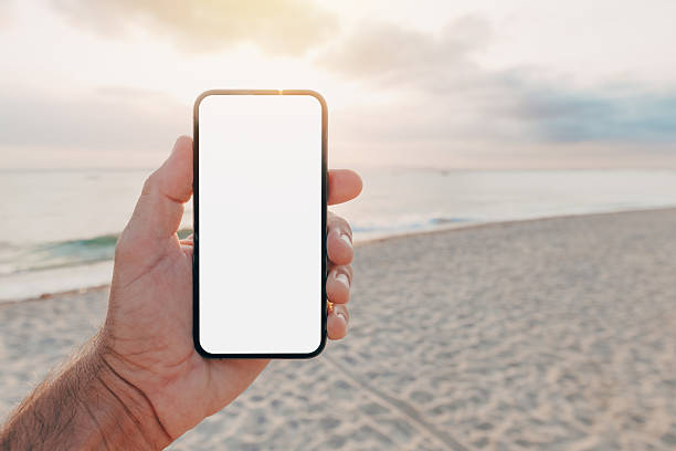 istock Hand holding smartphone with blank screen at beach during sunset, app or web interface mockup in natural outdoor lighting. 2228519008