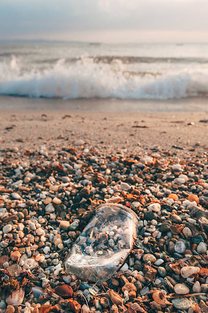 Plastic bottle waste on a pebble beach with ocean waves in the background. Coastal pollution concept with marine debris and environmental impact theme.