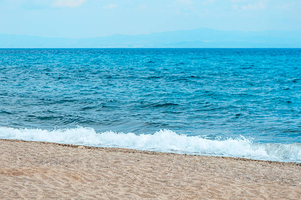 istock Gentle ocean waves lapping onto a sandy beach with a distant horizon and soft blue sky. The peaceful seascape captures the tranquility of a summer coastal scene. 2228519164