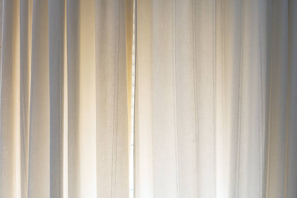 istock Sheer beige curtains with vertical stitching details softly illuminated by natural daylight. Minimalist interior decor with calming, warm tones. 2228519187