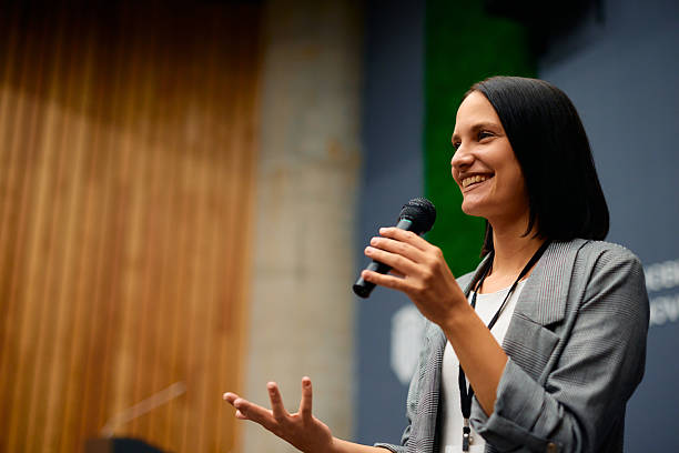 istock Smiling businesswoman speaking into microphone during conference 2228519643