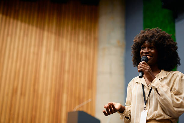 istock Young woman giving a speech holding a microphone in a conference room 2228519748