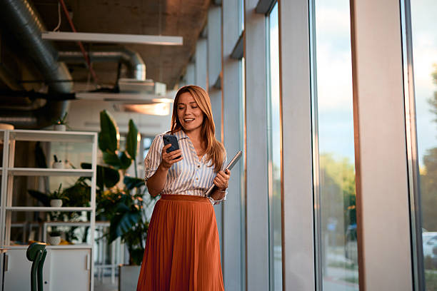istock Businesswoman walking in modern office using smartphone and holding tablet 2228523217