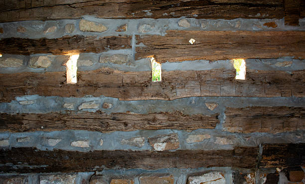 Interior of an old log cabin with rifle holes or slit ventilators constructed of wood planks, cement and rocks.