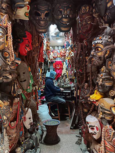 Kathmandu, Nepal - December 28, 2023
A person is seen playing a traditional musical instrument amidst a vibrant and intricate display of masks and artifacts in Kathmandu, Nepal. The narrow alley is lined with colorful masks, beads, and sculptures that reflect the rich cultural heritage of the region. The assortment of masks, featuring various human and animal faces, creates a captivating and immersive atmosphere. The individual, dressed in a hoodie, is focused on playing the instrument, contributing to the lively artistic scene of Kathmandu's bustling markets and craftsmanship. The scene captures the essence of Nepal's traditional arts and crafts, offering a glimpse into the city's creative spirit and cultural depth.