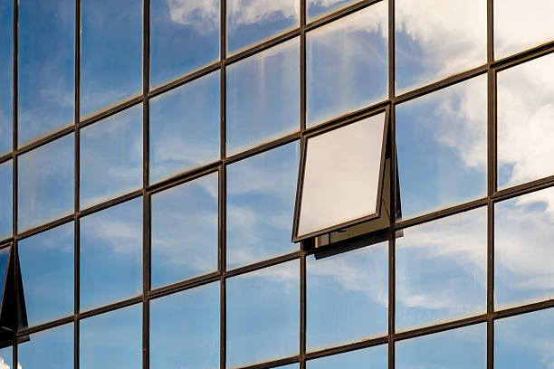 Modern glass building facade with open window reflecting blue sky and white clouds, symbolizing ventilation and fresh air in architectural design