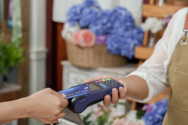 istock Customer making credit card payment by tapping on reader held by asian senior female florist operating floral shop decorated with fresh flowers as part of post retirement business 2228530690