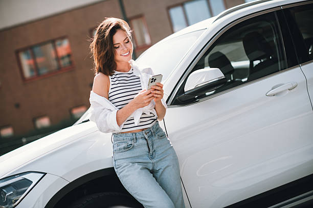 istock Young woman enjoying a sunny day outdoors, smiling while using her phone, leaning against a car 2228535000