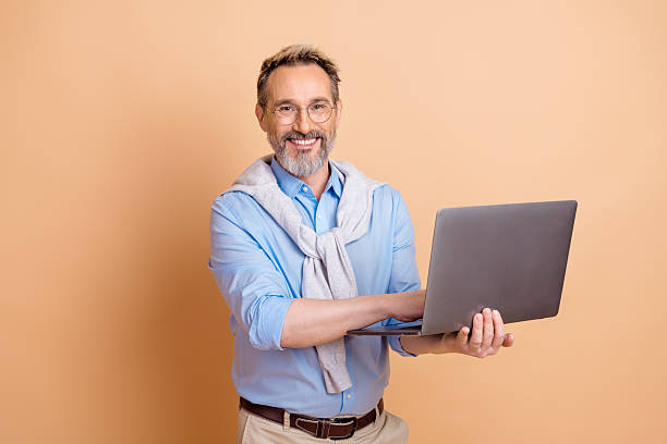 istock Confident mature businessman using a laptop while standing against a beige background showcasing professional elegance 2228536427