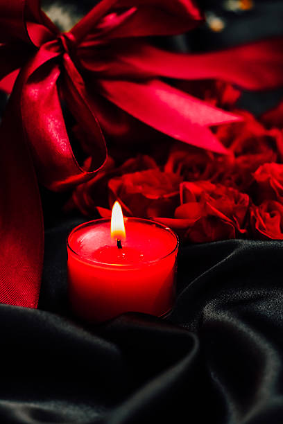 istock Elegant red candle surrounded by roses and ribbon on a black background for romantic settings 2228540340