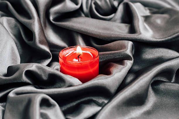 istock Red candle glowing on elegant black satin fabric in a serene setting for relaxation 2228540373